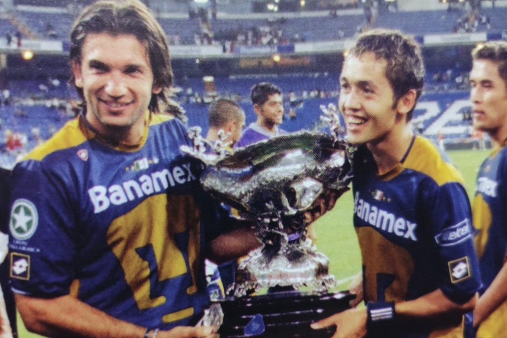 Dos futbolistas sosteniendo un trofeo en el estadio Santiago Bernabéu, con una expresión de alegría y triunfo.