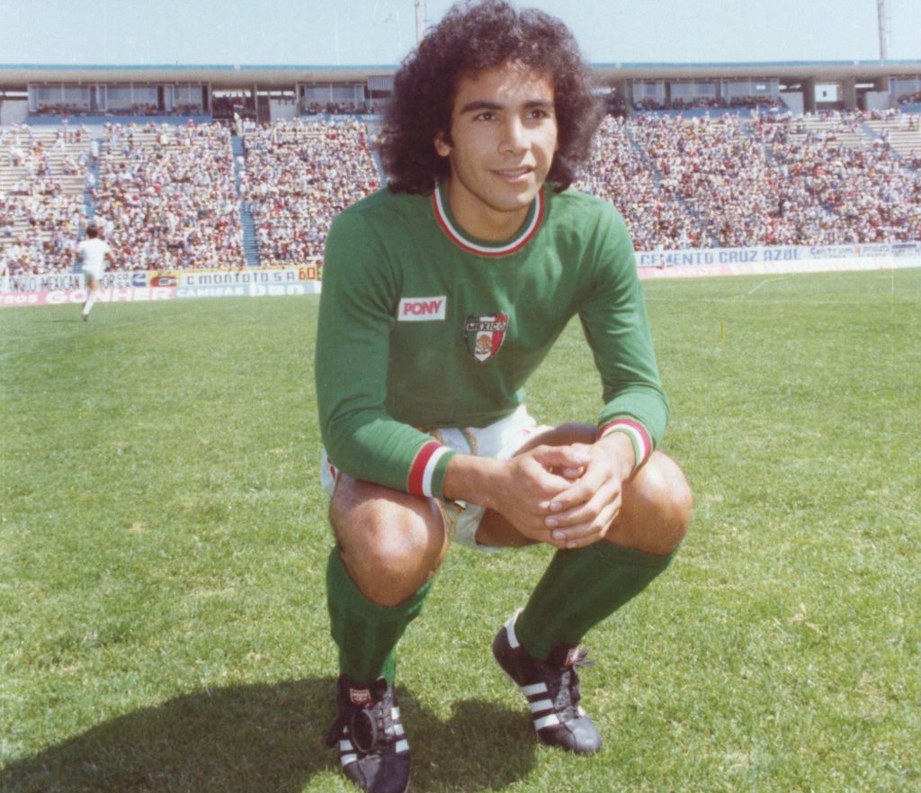 Futbolista mexicano posando en el campo de juego, vistiendo un uniforme verde de la selección nacional con el logo de la marca de ropa deportiva 'Pony'.