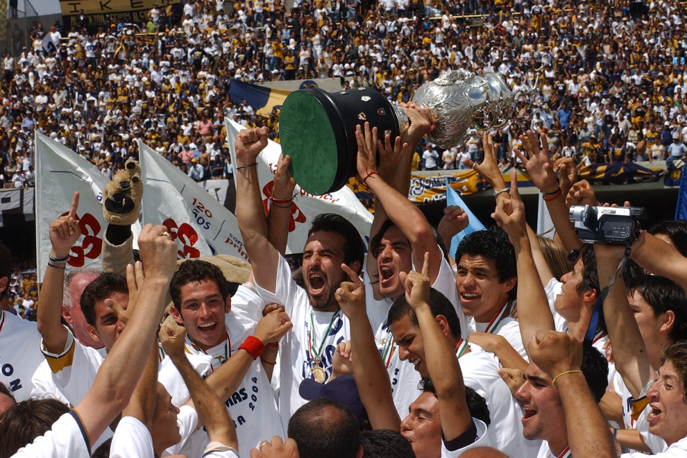 Jugadores del equipo Pumas celebrando con el trofeo en un estadio lleno de aficionados.